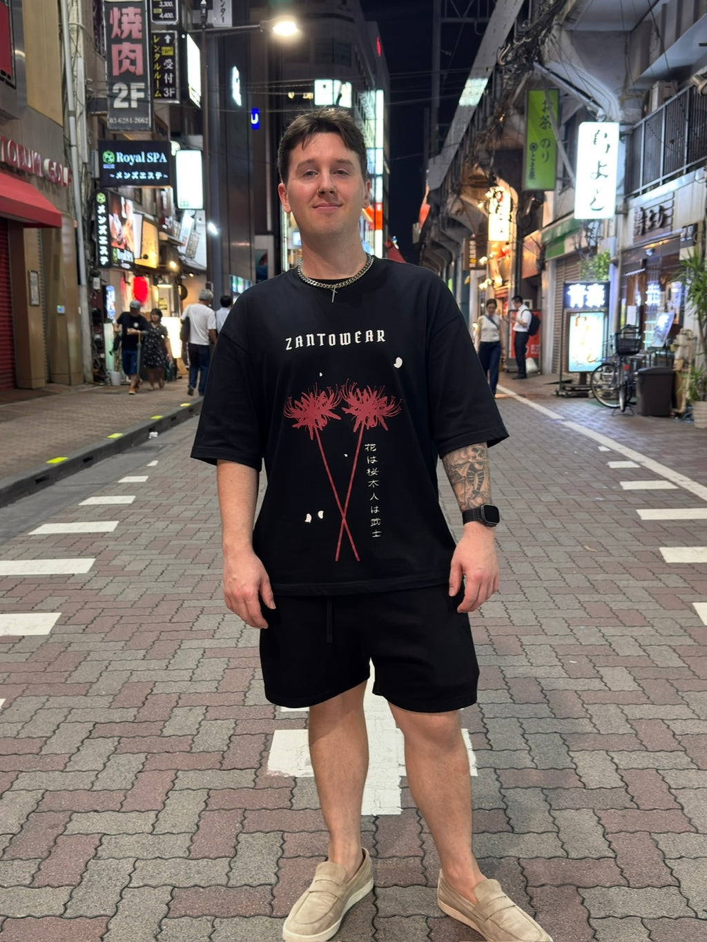 Person wearing a black t-shirt with Japanese spider lily on a street in an urban setting